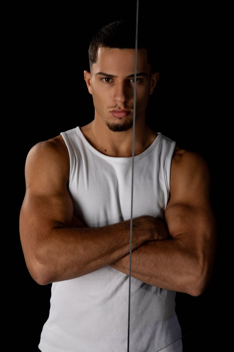 Mann im weissen Tanktop mit verschränkten Armen, eine Glaskante teilt sein Gesicht